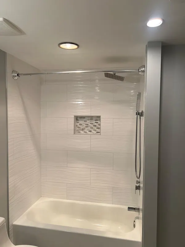 Bathtub and shower with white textured tile and a mosaic niche