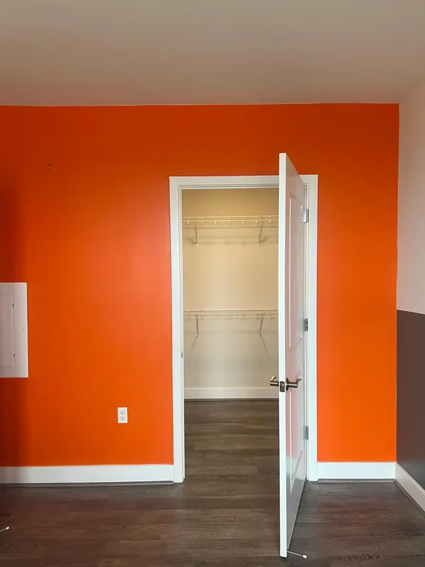 Bedroom with a bold orange accent wall, plank flooring and a walk-in closet