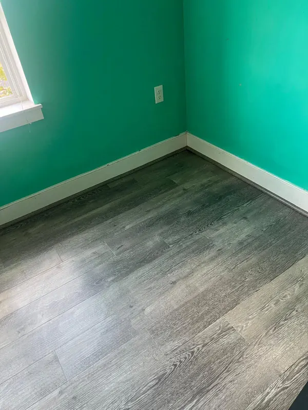 Gray plank flooring in a bedroom with teal walls and white baseboards