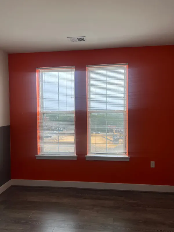 Room with red walls, two windows with blinds and dark plank flooring