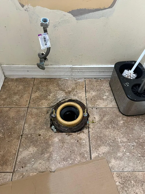 Toilet flange and water supply stub exposed in a bathroom with a damaged wall